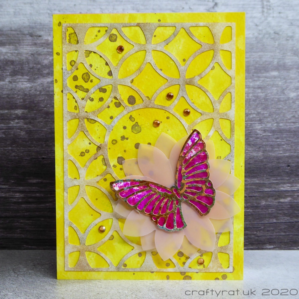 A card with a pink butterfly on a vellum flower on a yellow background topped with a curvy trellis pattern.