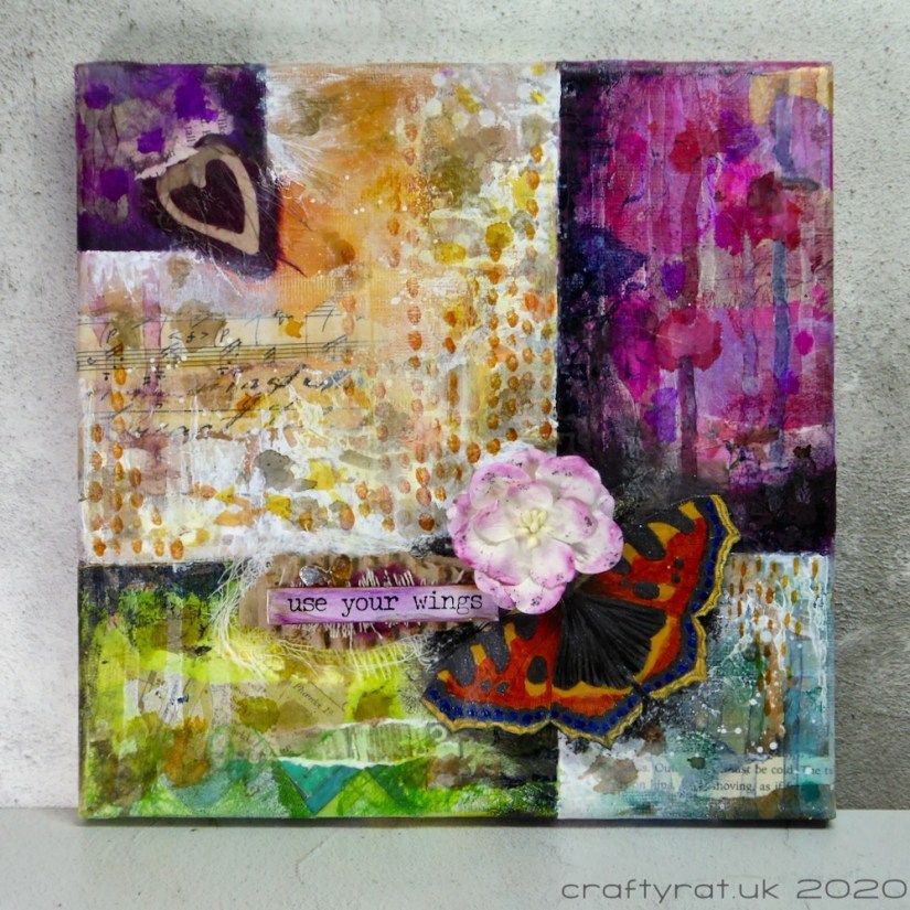 A mixed media canvas divided into a grid with panels in purples, greens, blues and neutral. It has a focal element comprising a butterfly, flower and the words "use your wings". 