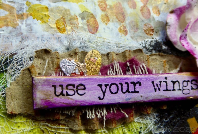 A close-up of the words "use your wings" with a small gilded heart tucked behind them.