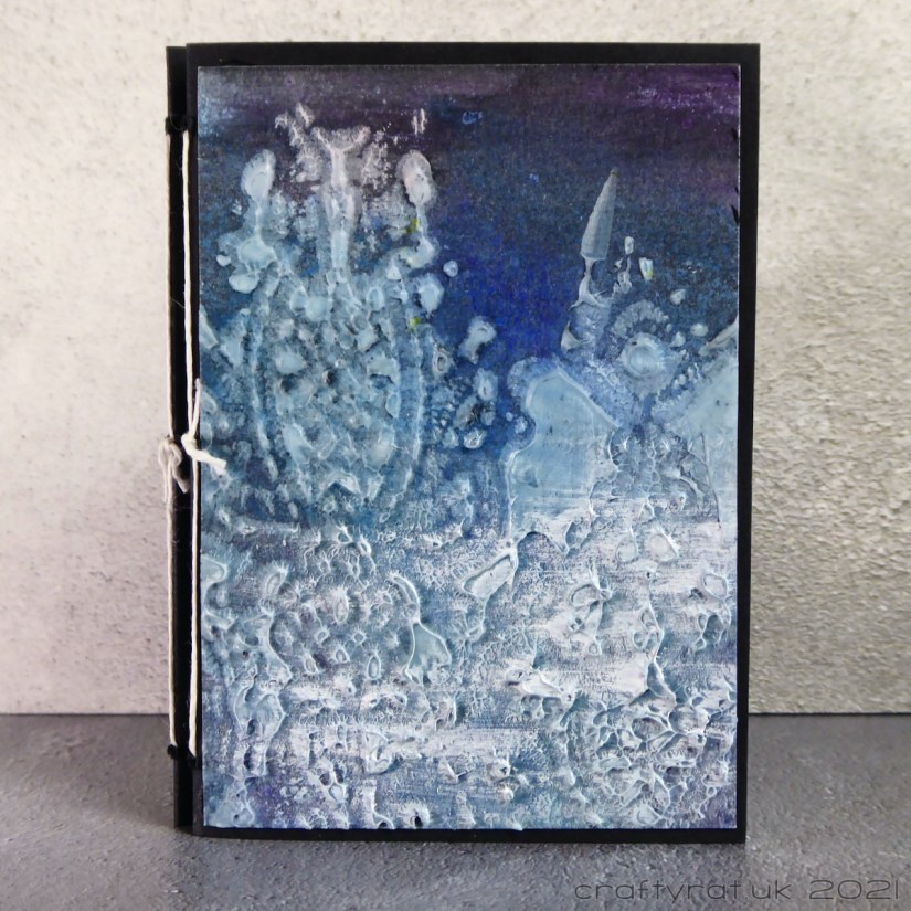 The cover of a small journal, dark blue in colour with white stencilled texture paste over two-thirds of the cover.
