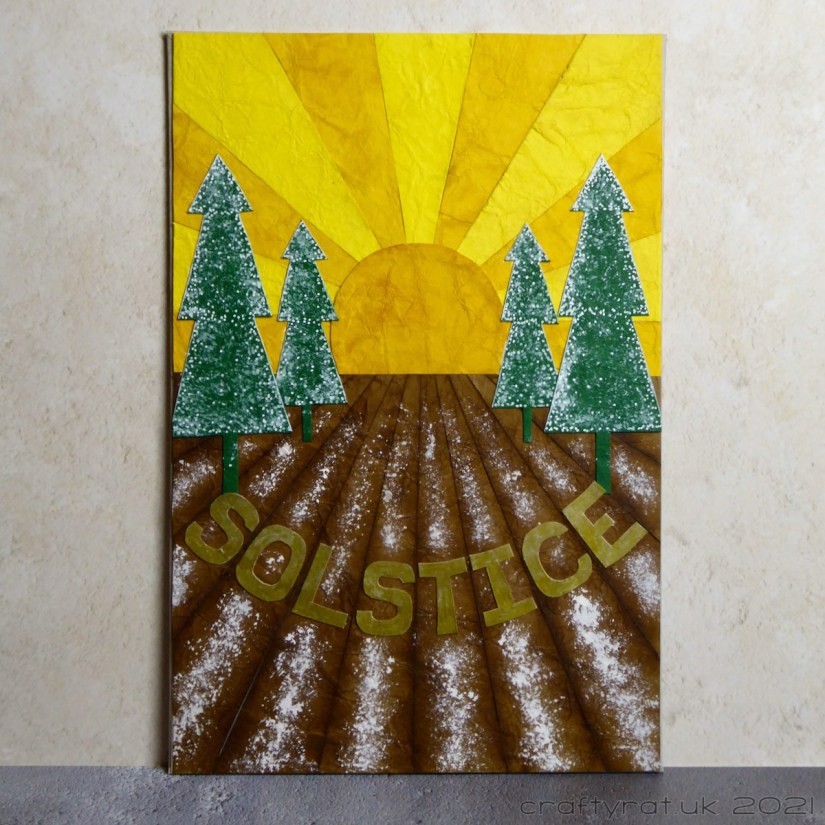 A geometric paper-pieced Solstice journal page with the sun rising over a snowy field with fir trees.